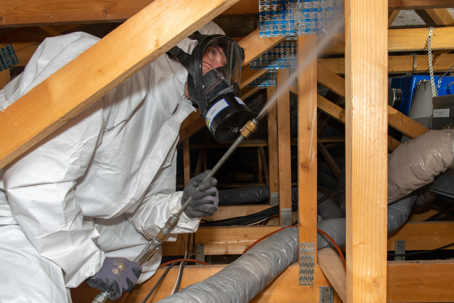 Technicien désinfectant un grenier masqué en combinaison.